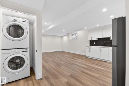 Open concept living space featuring wood-finish flooring, recessed lighting, and a kitchen area with white cabinetry, a dark backsplash, and a built-in refrigerator - 5308 103A Avenue, Edmonton, AB - Indoor Photo Showing Laundry Room