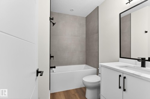 Contemporary bathroom with a white bathtub and shower featuring matte black fixtures, set against large format wall tiles - 5308 103A Avenue, Edmonton, AB - Indoor Photo Showing Bathroom