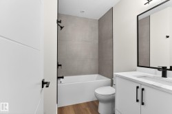 Contemporary bathroom with a white bathtub and shower featuring matte black fixtures, set against large format wall tiles - 
