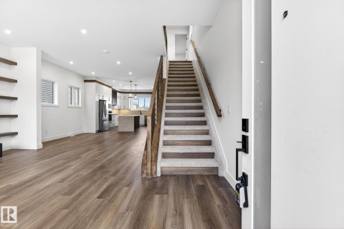 Open-concept living space featuring wood-finish flooring, recessed lighting, floating wall shelving, a carpeted staircase with wood railing, and a kitchen with an island - 5308 103A Avenue, Edmonton, AB - Indoor Photo Showing Other Room