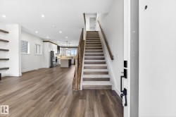 Open-concept living space featuring wood-finish flooring, recessed lighting, floating wall shelving, a carpeted staircase with wood railing, and a kitchen with an island - 