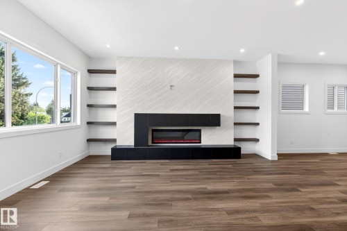 Statement fireplace wall featuring a modern electric fireplace, integrated media console, and flanking open shelving - 5308 103A Avenue, Edmonton, AB - Indoor Photo Showing Other Room With Fireplace