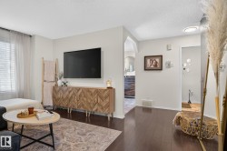 Living area featuring dark wood-finish flooring, light neutral wall tones, and a window with blinds and sheer curtains - 