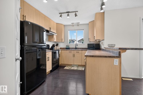 Kitchen featuring wood-finish flooring, light wood cabinetry, black appliances, dark countertops, and a double-tier breakfast bar - 191 Brookview Place, Stony Plain, AB - Indoor Photo Showing Kitchen