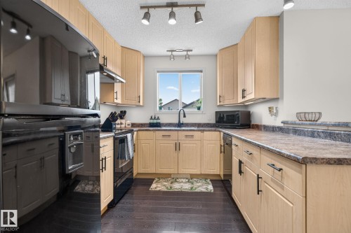 U-shaped kitchen featuring light wood-finish cabinetry with matte black hardware, dark wood-finish flooring, a double basin sink with a black faucet, and track lighting - 191 Brookview Place, Stony Plain, AB - Indoor Photo Showing Kitchen