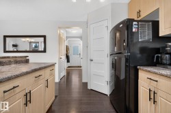 Kitchen featuring light wood-finish cabinetry with black hardware, stone-look countertops, and recessed lighting - 