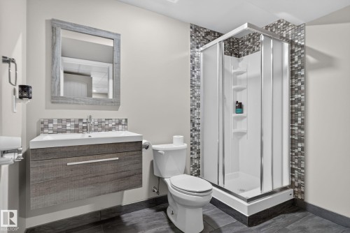 Bathroom featuring a floating wood-finish vanity with an integrated sink, a rectangular framed mirror, a tiled backsplash, a corner shower with glass enclosure, and dark tile flooring - 191 Brookview Place, Stony Plain, AB - Indoor Photo Showing Bathroom