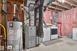 Utility area featuring a water heater, furnace, and laundry appliances with exposed ceiling joists and wall insulation - 
