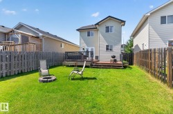 Spacious backyard featuring a lush lawn, privacy fencing, a two-story home with light-colored siding, and a multi-level wooden deck with dark railings - 