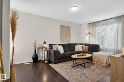 Living area featuring dark wood-finish flooring, a large window with blinds and sheer curtains, and a ceiling-mounted light fixture - 