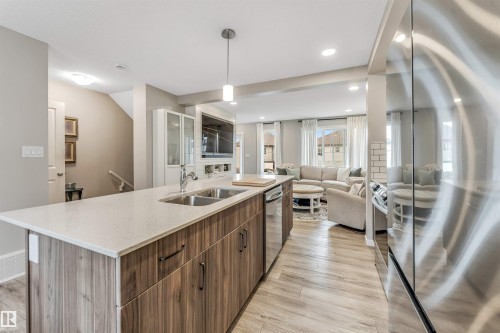 Kitchen island featuring a dual-basin stainless steel sink, light-toned countertop, and wood-finish cabinetry - #25 1530 Tamarack Bv Nw, Edmonton, AB - Indoor Photo Showing Kitchen With Double Sink With Upgraded Kitchen