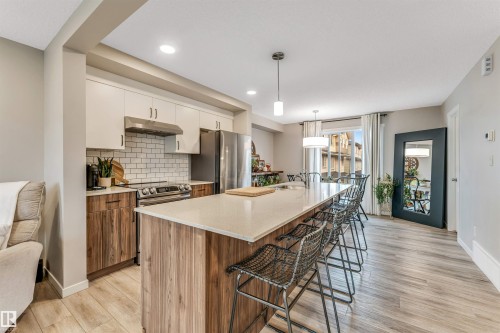 Spacious kitchen featuring a large island with seating, a stainless steel appliance suite, white subway tile backsplash, and light wood-finish flooring - #25 1530 Tamarack Bv Nw, Edmonton, AB - Indoor Photo Showing Kitchen With Upgraded Kitchen