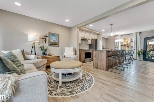 Open-concept living space with light wood-finish flooring, recessed lighting, a kitchen island with seating, a subway tile backsplash, and a large window with white curtains - #25 1530 Tamarack Bv Nw, Edmonton, AB - Indoor Photo Showing Living Room