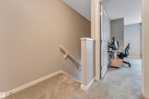 Carpeted hallway with a neutral color palette, featuring a white handrail and a painted wooden newel post - #25 1530 Tamarack Bv Nw, Edmonton, AB - Indoor Photo Showing Other Room