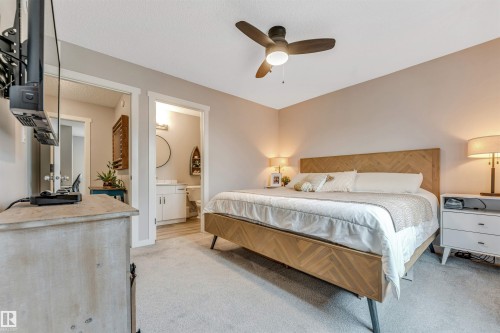 Carpeted bedroom featuring a ceiling fan with integrated lighting, two framed doorways, and neutral wall tones - #25 1530 Tamarack Bv Nw, Edmonton, AB - Indoor Photo Showing Bedroom