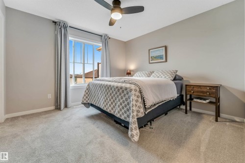 Bedroom featuring light gray wall paint, neutral carpet flooring, a large window with white trim, and a ceiling fan with integrated lighting - #25 1530 Tamarack Bv Nw, Edmonton, AB - Indoor Photo Showing Bedroom