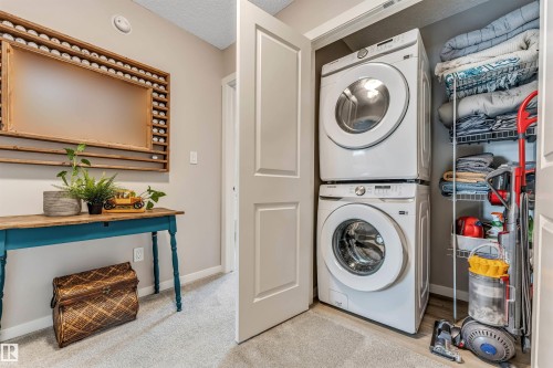 Dedicated laundry closet featuring a stacked washer and dryer, adjacent to a hallway with neutral wall paint and carpet flooring - #25 1530 Tamarack Bv Nw, Edmonton, AB - Indoor Photo Showing Laundry Room