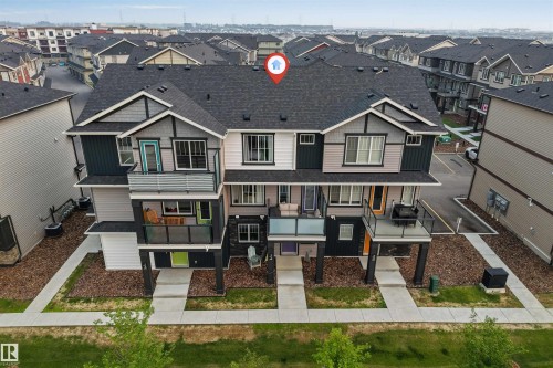 Contemporary multi-level townhome featuring a dark shingle roof, two private balconies with glass railings, and a distinct facade with varying siding materials - #25 1530 Tamarack Bv Nw, Edmonton, AB - Outdoor With Facade