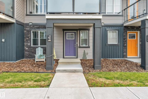 Entryway featuring a purple door, concrete walkway, porch overhang with dark pillars, and wood-chip landscaping - #25 1530 Tamarack Bv Nw, Edmonton, AB - Outdoor With Facade