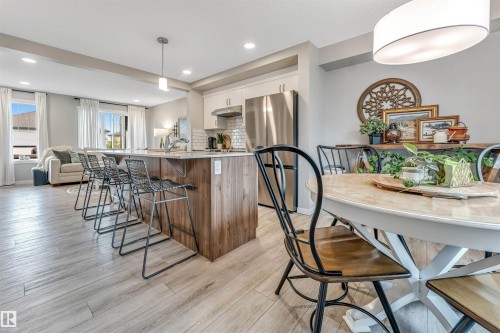 Open-concept kitchen and dining area featuring light wood-finish flooring, a kitchen island with seating, white shaker-style cabinetry, and stainless steel appliances - #25 1530 Tamarack Bv Nw, Edmonton, AB - Indoor Photo Showing Dining Room