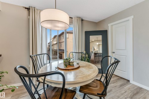 Dining area featuring a contemporary drum pendant light, wood-finish flooring, a white paneled door, and neutral wall tones - #25 1530 Tamarack Bv Nw, Edmonton, AB - Indoor Photo Showing Dining Room