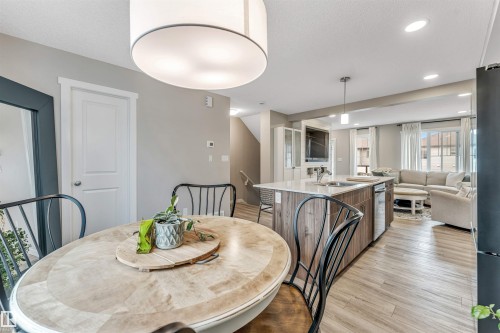 Open-concept living space featuring wood-finish flooring, a kitchen island with stone countertop and integrated sink, recessed lighting, and a built-in entertainment center - #25 1530 Tamarack Bv Nw, Edmonton, AB - Indoor Photo Showing Dining Room