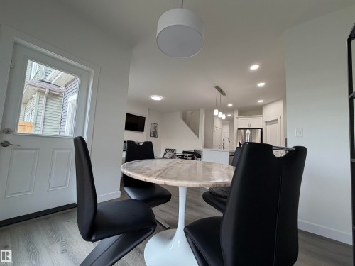 Modern kitchen and dining area featuring light wood-finish flooring, white walls, and recessed lighting - 3631 213 Street Nw, Edmonton, AB - Indoor