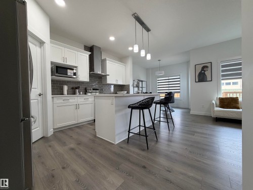 Modern kitchen featuring white shaker cabinetry, stainless steel appliances, a subway tile backsplash, a kitchen island with seating, and wood-finish flooring - 3631 213 Street Nw, Edmonton, AB - Indoor Photo Showing Kitchen With Upgraded Kitchen