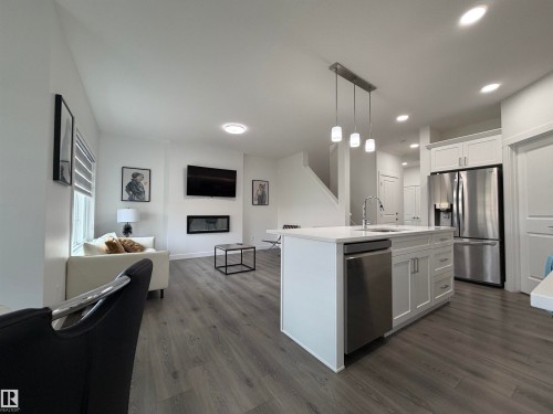 Open-concept living space featuring a kitchen island with pendant lighting, stainless steel appliances, wood-finish flooring, and a modern fireplace - 3631 213 Street Nw, Edmonton, AB - Indoor Photo Showing Kitchen