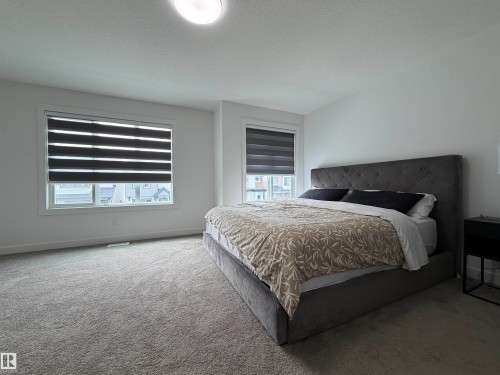 Spacious room featuring light gray carpet flooring, white walls, and two windows equipped with striped roller blinds - 3631 213 Street Nw, Edmonton, AB - Indoor Photo Showing Bedroom