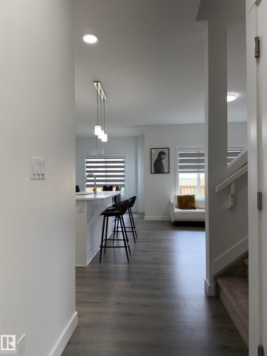 Contemporary interior featuring recessed lighting, a modern linear pendant light fixture, wood-finish flooring, a kitchen island with seating, and a staircase with carpeting and a white handrail - 3631 213 Street Nw, Edmonton, AB - Indoor Photo Showing Other Room