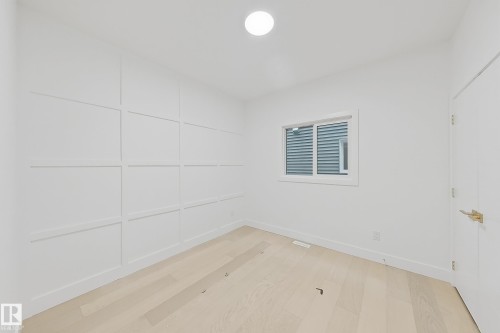Bright interior space featuring a grid accent wall, wood-finish flooring, a contemporary ceiling light fixture, and a white window frame - 8423 Mayday Link Link Sw, Edmonton, AB - Indoor Photo Showing Other Room