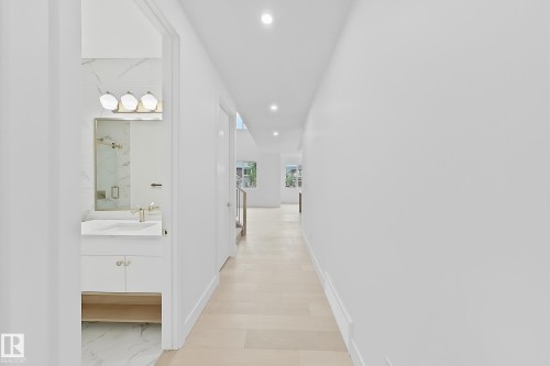 Hallway with wood-finish flooring, recessed lighting, and a bathroom featuring a modern vanity with a gold-tone faucet, a mirror, and a three-light fixture - 8423 Mayday Link Link Sw, Edmonton, AB - Indoor Photo Showing Bathroom