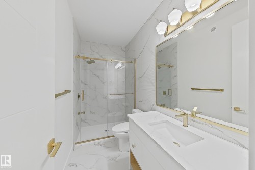 Contemporary bathroom featuring a spacious vanity with integrated sink, gold-toned fixtures, a large mirror, a glass-enclosed shower with a rain showerhead, and white marble-look tile flooring - 8423 Mayday Link Link Sw, Edmonton, AB - Indoor Photo Showing Bathroom