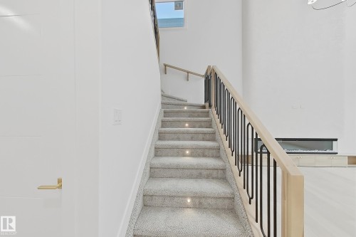 Staircase featuring light-toned carpet, recessed stair lighting, light wood handrails, and black metal balusters - 8423 Mayday Link Link Sw, Edmonton, AB - Indoor Photo Showing Other Room