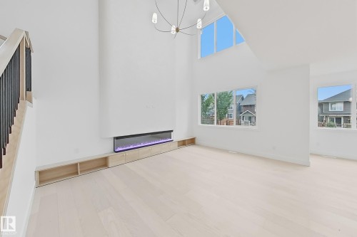 Spacious living area featuring high ceilings, light wood-finish flooring, and an electric fireplace with built-in cabinetry - 8423 Mayday Link Link Sw, Edmonton, AB - Indoor Photo Showing Other Room