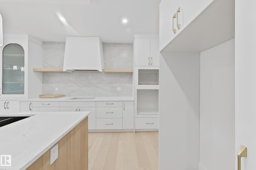 Kitchen featuring white cabinetry, quartz countertops, a stone slab backsplash, wood-finish flooring, and a built-in range hood - 8423 Mayday Link Link Sw, Edmonton, AB - Indoor