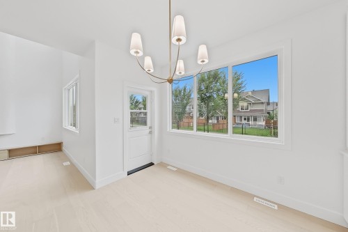 Bright interior space featuring a multi-pane window wall, light wood-finish flooring, a contemporary chandelier, a white half-lite exterior door, and high ceilings - 8423 Mayday Link Link Sw, Edmonton, AB - Indoor Photo Showing Other Room