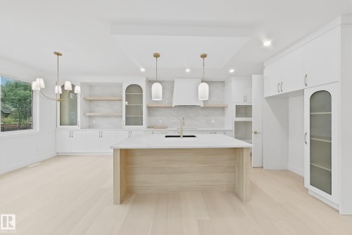 Kitchen featuring a light wood-finish island with a built-in sink, white cabinetry with gold-tone hardware, a white tile backsplash, and light wood-finish flooring - 8423 Mayday Link Link Sw, Edmonton, AB - Indoor Photo Showing Kitchen With Upgraded Kitchen