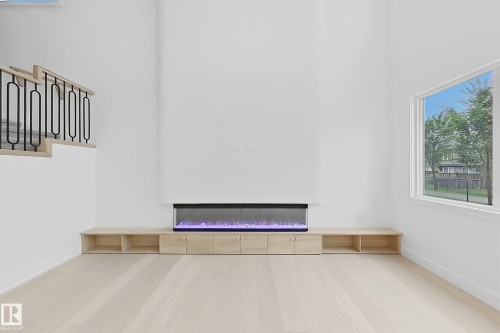 Open living area featuring a linear electric fireplace with custom wood-finish cabinetry - 8423 Mayday Link Link Sw, Edmonton, AB - Indoor Photo Showing Other Room