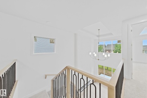 Two-story foyer featuring an open staircase with wood handrails, decorative metal balusters, a contemporary chandelier, and large windows - 8423 Mayday Link Link Sw, Edmonton, AB - Indoor Photo Showing Other Room