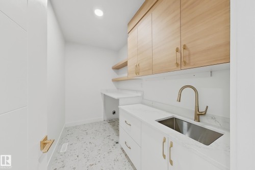 Laundry area featuring light wood-finish cabinetry, a stainless steel sink with a brass-tone faucet, and white countertops - 8423 Mayday Link Link Sw, Edmonton, AB - Indoor Photo Showing Kitchen
