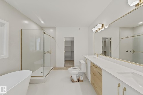 Bright bathroom featuring a freestanding tub, glass-enclosed shower, dual vanity with undermount sinks, and a long mirror with gold-finished accents - 8423 Mayday Link Link Sw, Edmonton, AB - Indoor Photo Showing Bathroom