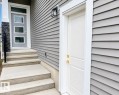 Exterior featuring horizontal siding, a contemporary entry door with three glass panels, a stone-accented pillar, and concrete steps with an integrated black metal handrail - 8423 Mayday Link Link Sw, Edmonton, AB  - Outdoor With Exterior 