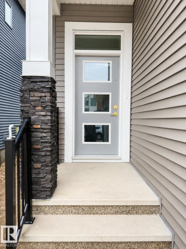 Contemporary entry featuring a light grey door with three rectangular lites, a transom window, and brass-finish hardware - 8423 Mayday Link Link Sw, Edmonton, AB - Outdoor With Exterior