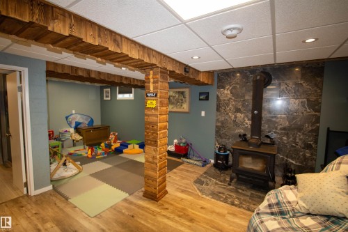 Finished lower level with wood-finish flooring, drop ceiling with recessed lighting, and an accent wall featuring a wood-burning stove on a stone-look hearth - 5017 55 Ave, St. Paul Town, AB - Indoor With Fireplace