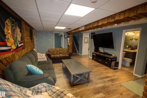 Lower level recreation area featuring wood-finish flooring, wood paneling, recessed ceiling lights, and a full bathroom with a vanity and toilet - 5017 55 Ave, St. Paul Town, AB - Indoor