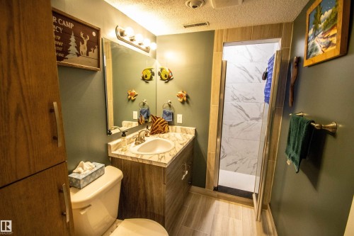 Bathroom featuring a wood-finish vanity with a built-in sink and countertop, a glass-enclosed shower with tiled walls, wood-finish flooring, and built-in vertical cabinetry - 5017 55 Ave, St. Paul Town, AB - Indoor Photo Showing Bathroom