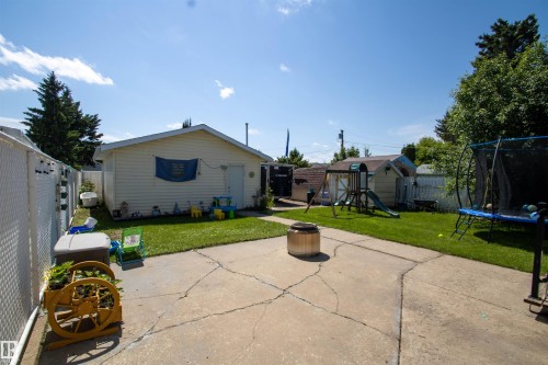 Expansive backyard featuring a concrete patio, a detached garage with vinyl siding, a chain-link fence, and a grassy lawn area - 5017 55 Ave, St. Paul Town, AB - Outdoor