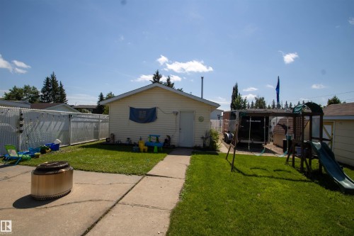 Expansive backyard featuring a detached garage with vinyl siding, a concrete patio, a manicured lawn, and a chain-link fence - 5017 55 Ave, St. Paul Town, AB - Outdoor